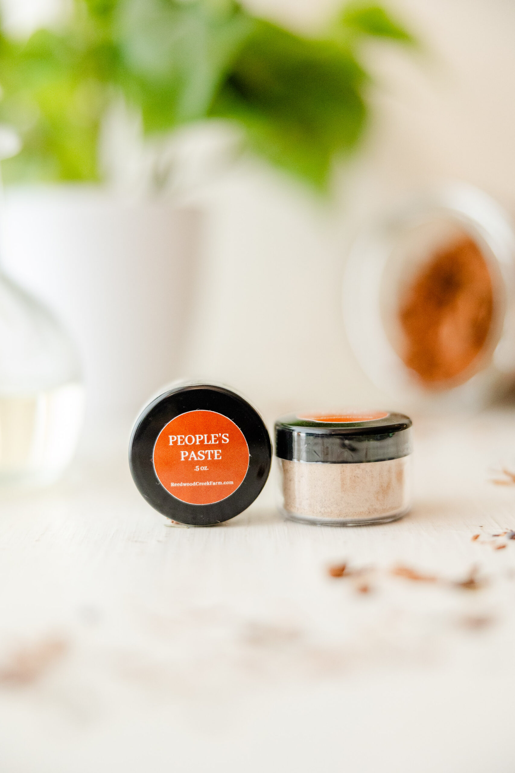 Image of People's Paste Powder on white table with house plant in background