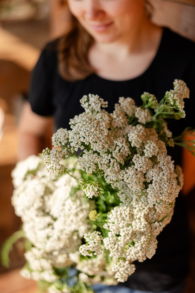 Woman smiling in the background while holding bouquet of yarrow flowers