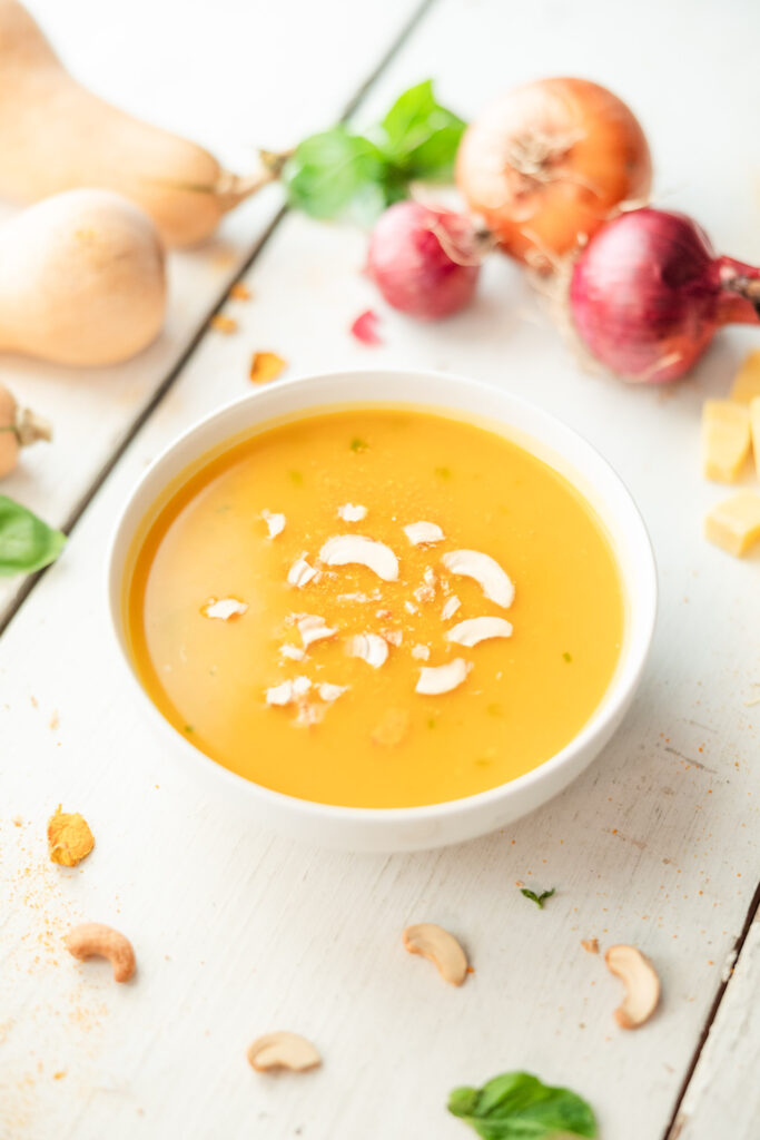 Easy Creamy butternut squash soup surrounded by butternut squashes and onions
