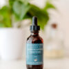 Image of Ashwagandha Tincture in 2 oz Amber Glass Bottle on White table with houseplant in background